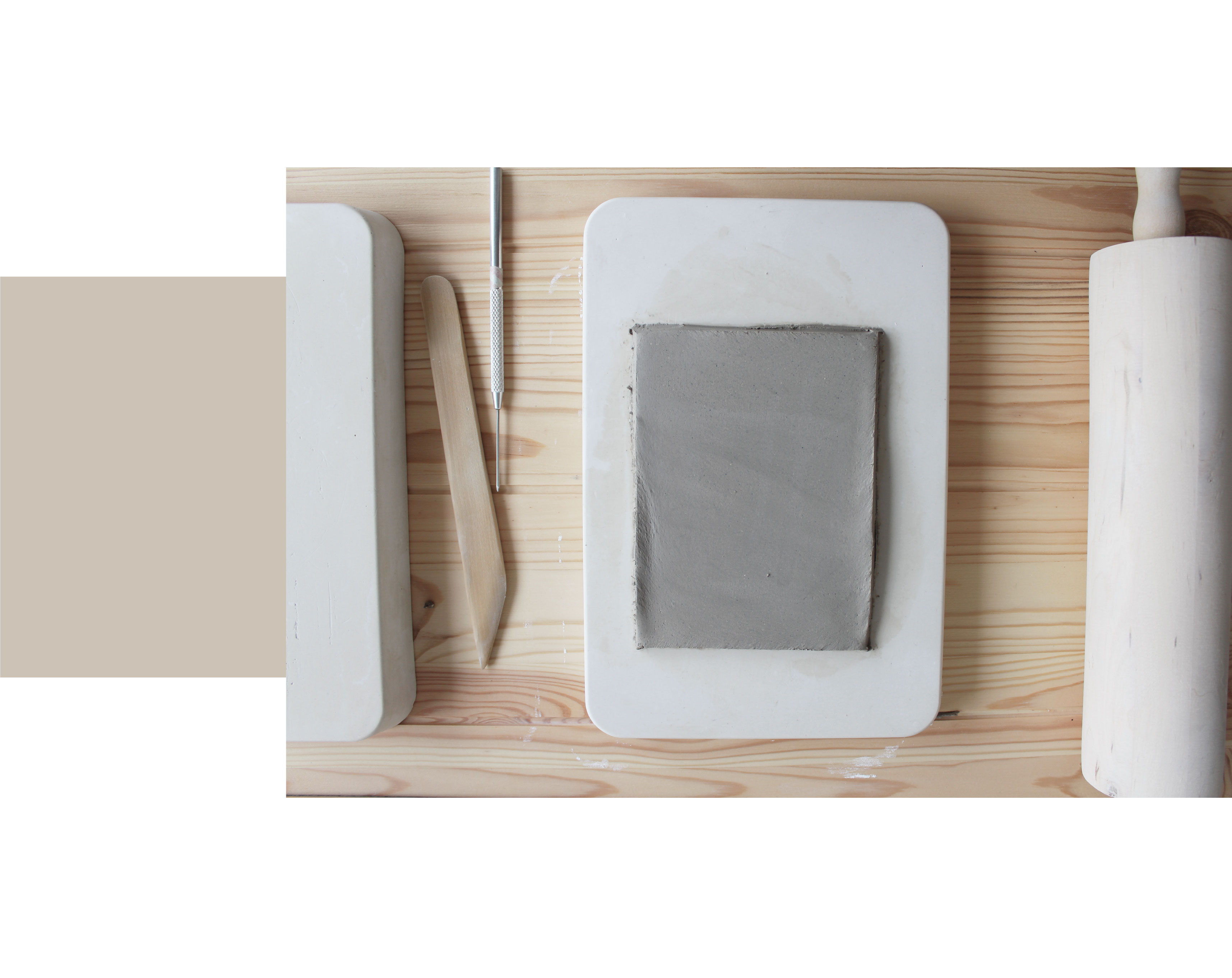 træ skrivebord med gips rektangel flagermus, en træ kagerulle, keramik værktøjer og en plade af grå ler rullet ind i en flad rektangel.